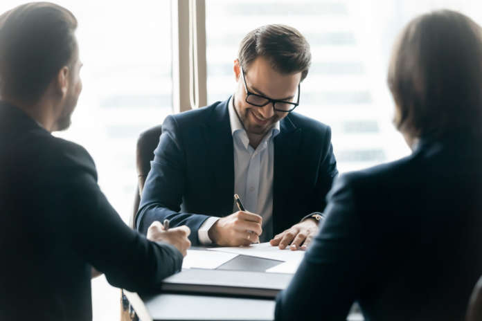 Smiling,Confident,Businessman,Wearing,Glasses,Signing,Contract,At,Group,Negotiations,