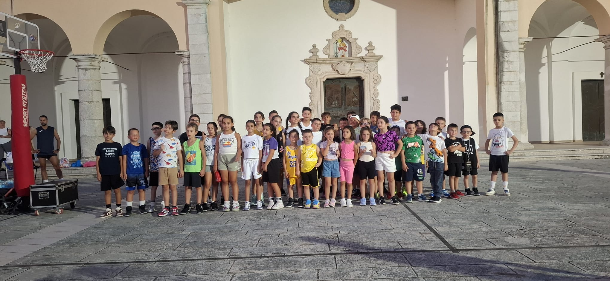 Bambini giocano a minibasket sul sagrato della Chiesa di San Rocco, con famiglie e volontari